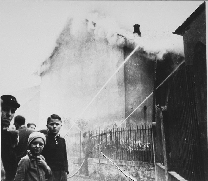 На утро после хрустальной ночи, местные жители смотрят как синагога разрушена огнем.